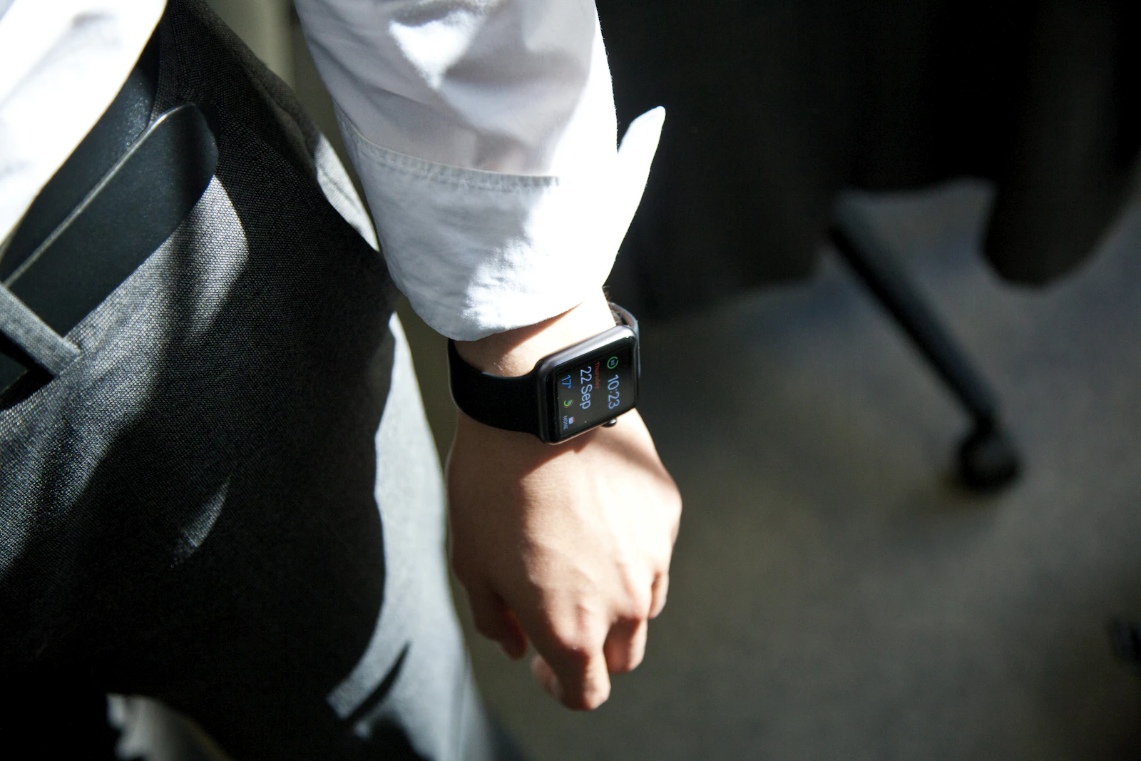 Apple Watch with a black band on a wrist beside a white shirt cuff