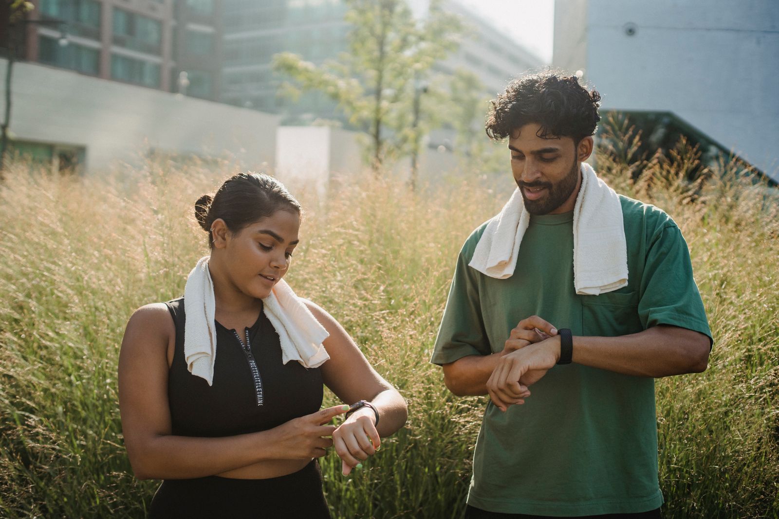Two people in sportswear checking their wristwatches outdoors