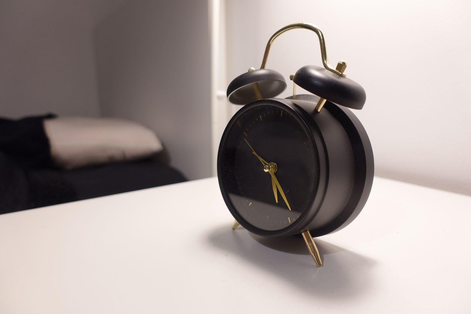 Black alarm clock on a white bedside table beside a bed